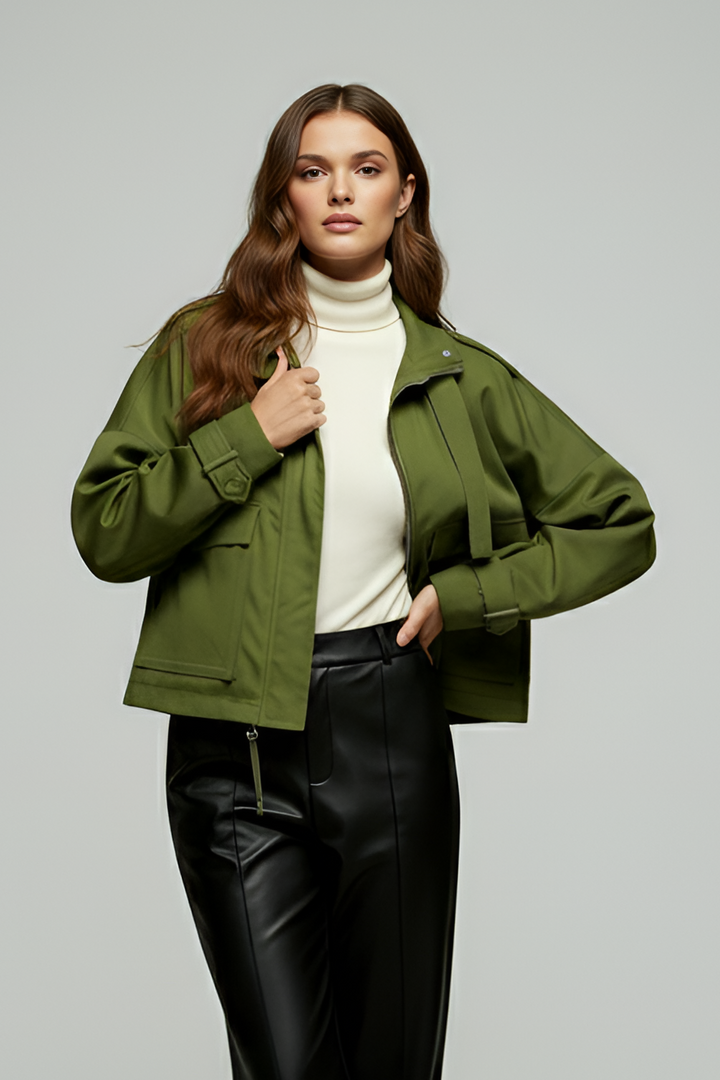 Woman wearing a green jacket and black pants on a gray background