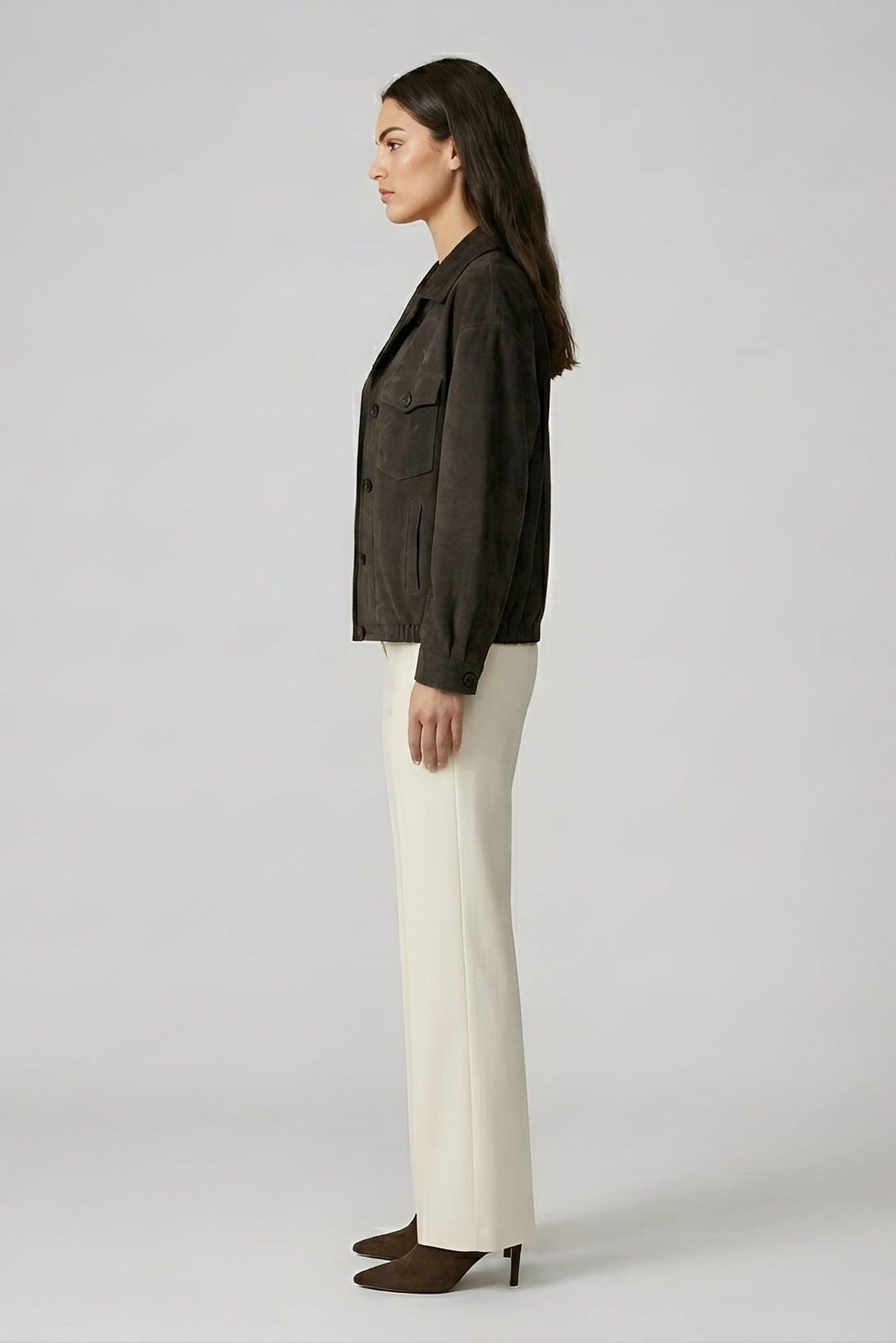 Woman wearing a dark jacket and white pants on a plain background
