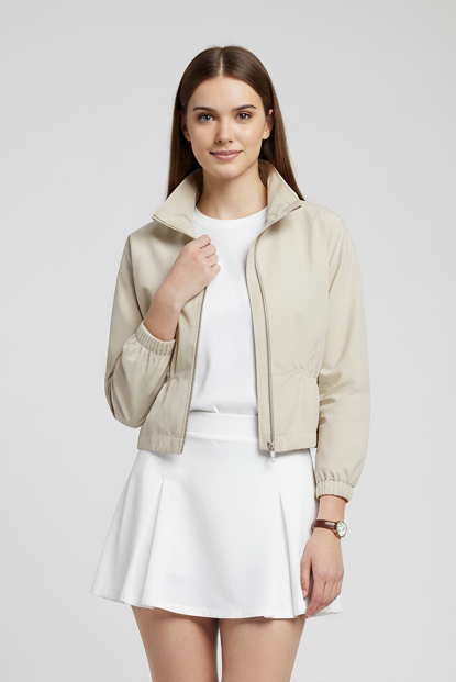 Woman wearing a beige jacket, white shirt, and skirt on a plain background