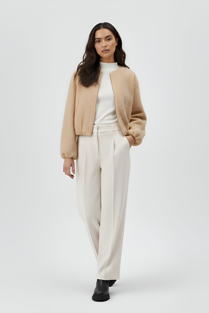 Woman wearing a beige cardigan, white top, and cream pants on a white background