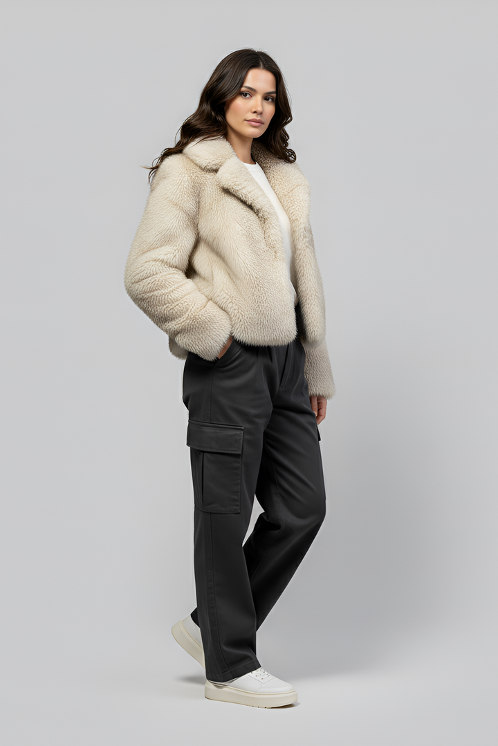 Woman wearing a beige fur coat and dark cargo pants on a gray background