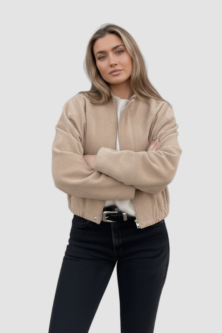 Woman wearing a beige jacket and black pants against a gray background