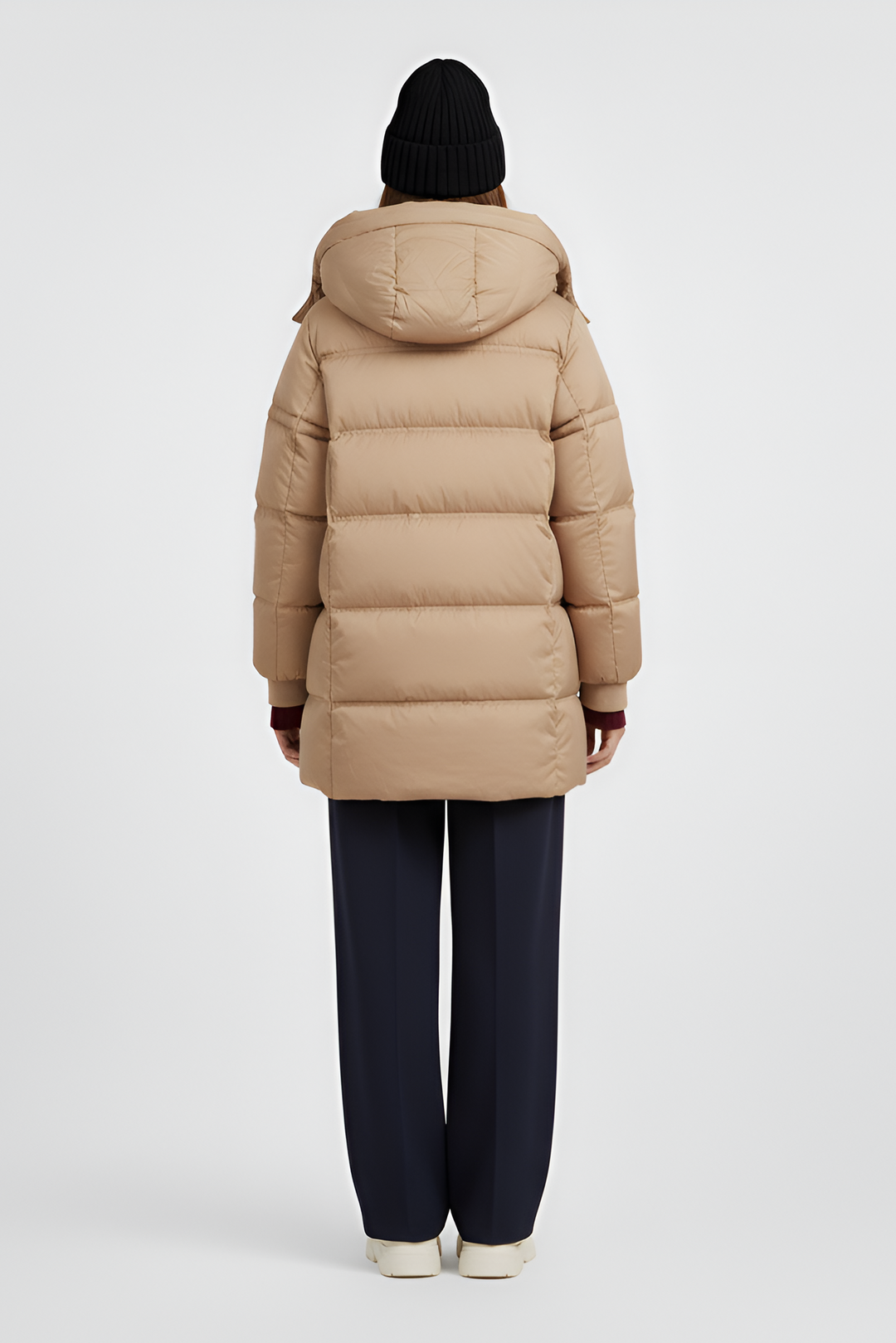 Woman wearing a beige puffer coat, sweater, and pants on a light gray background