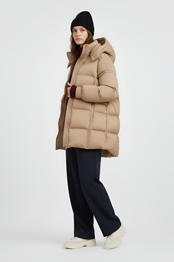 Woman wearing a beige puffer coat, sweater, and pants on a light gray background