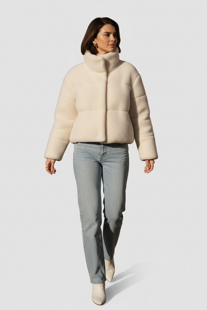 Woman wearing a beige puffer jacket and light blue jeans on a white background