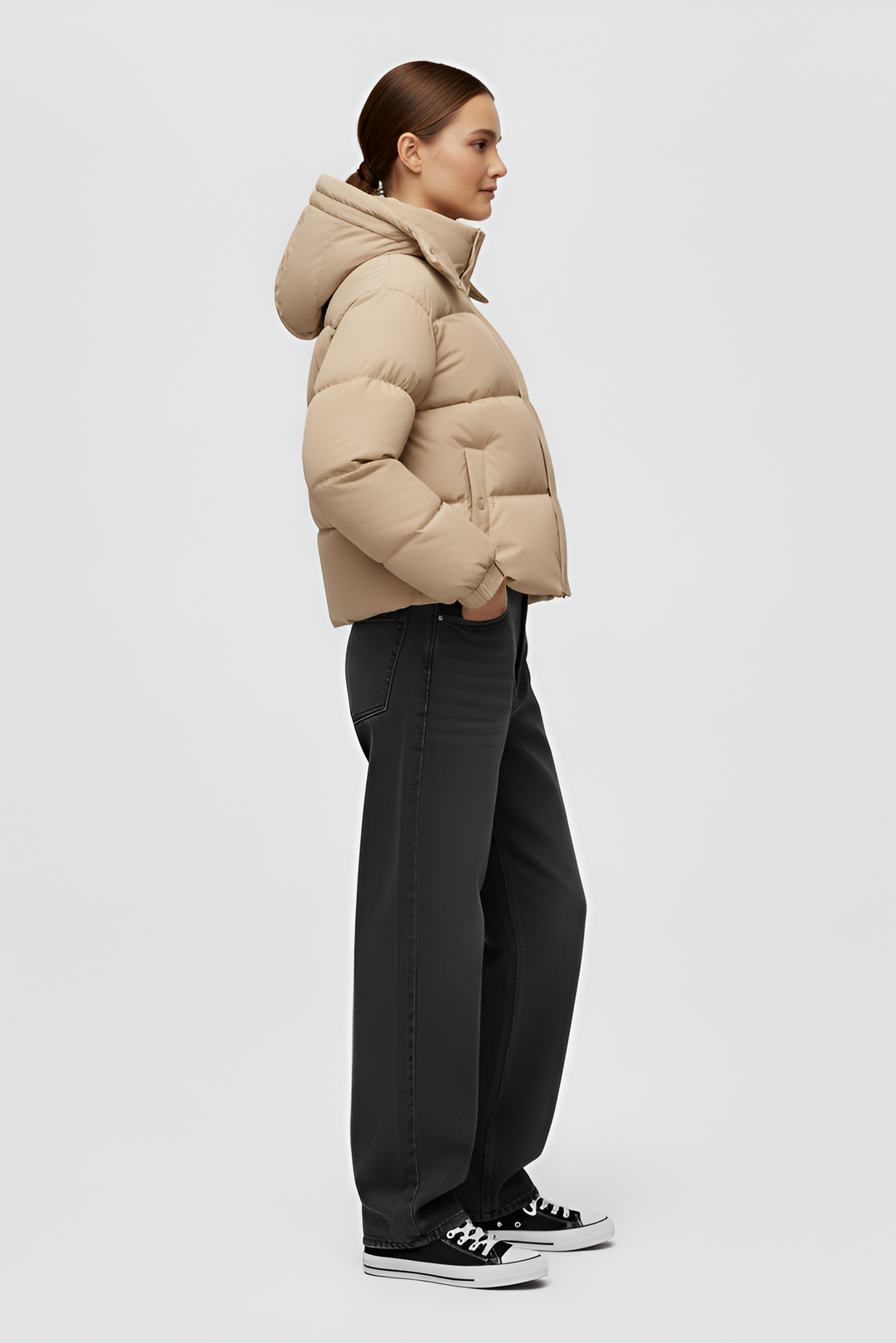 Woman wearing a beige puffer jacket and cap standing in an urban setting.