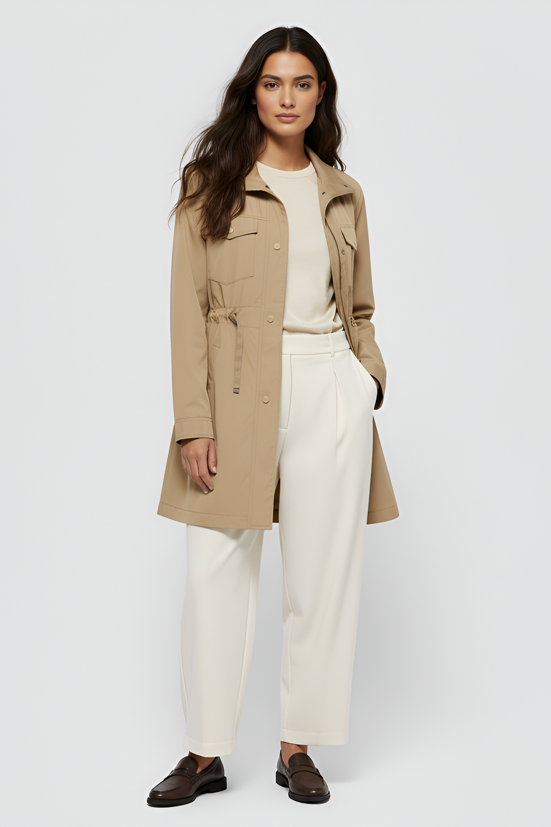 Woman wearing a beige trench coat over a white outfit on a light gray background