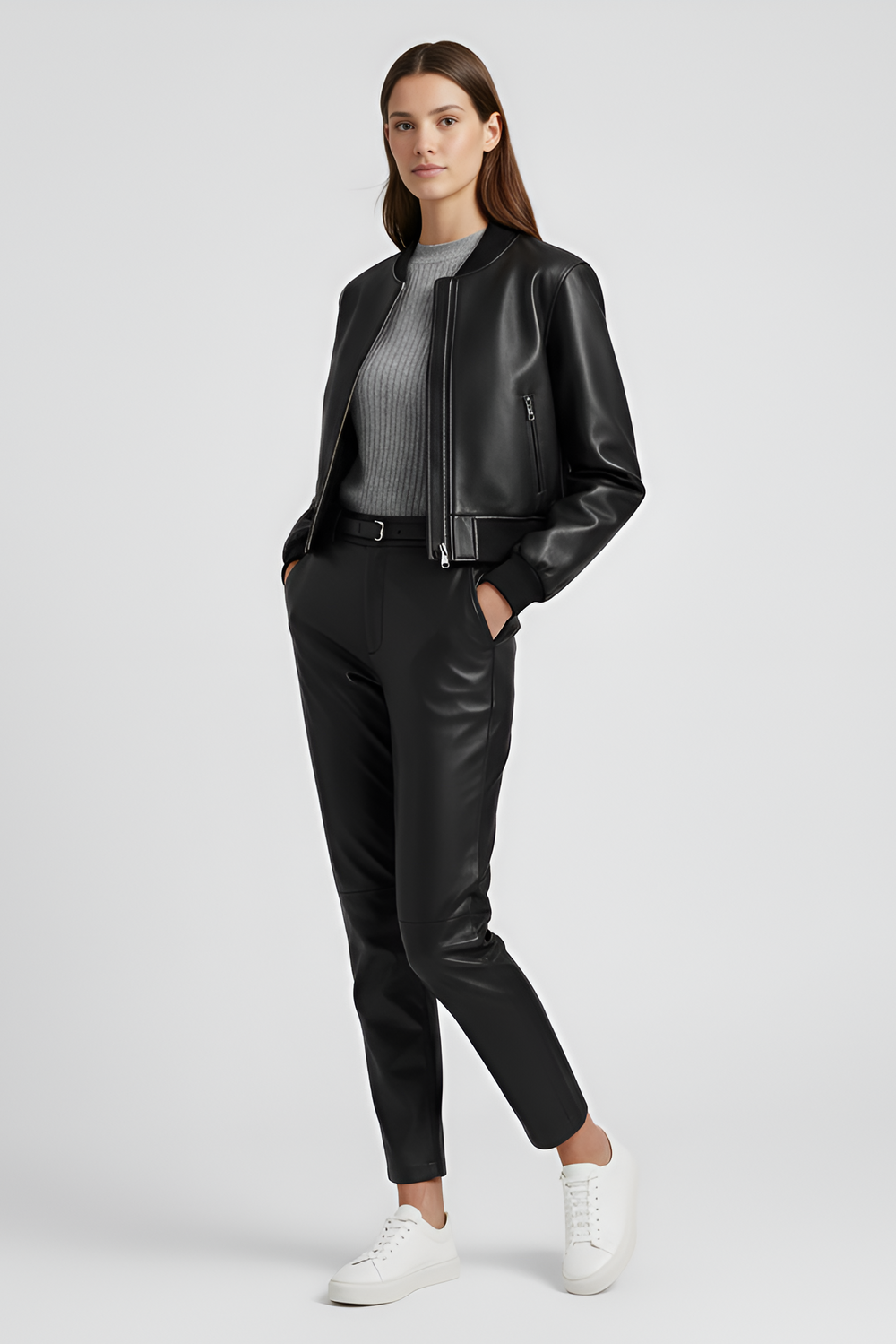 Woman wearing a black leather jacket, white top, blue jeans, and black boots on a gray background