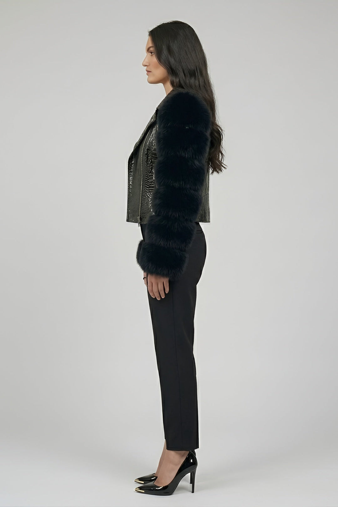 Woman wearing a black fur jacket and black pants on a gray background