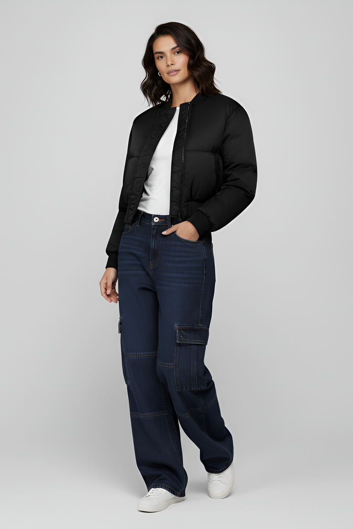 Woman wearing a black jacket and dark blue cargo pants on a light gray background
