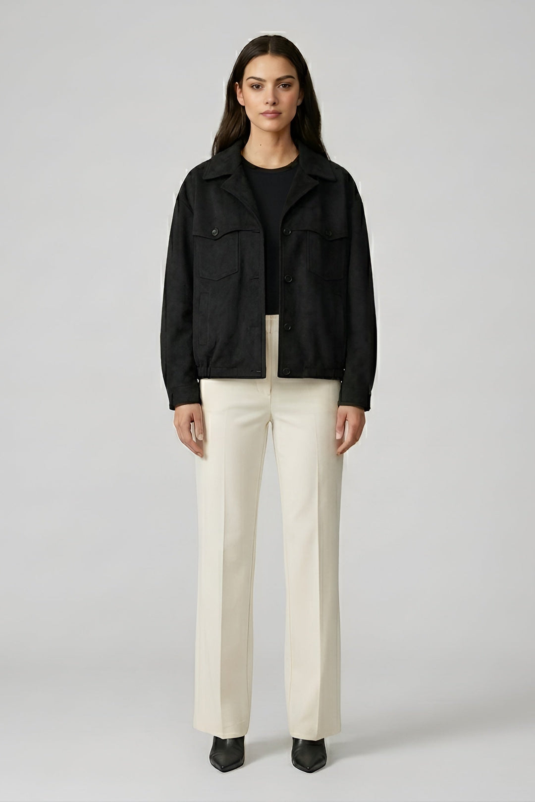 Woman wearing a black jacket and white pants on a gray background