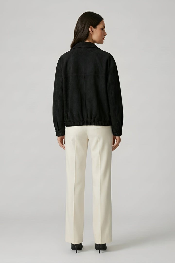 Woman wearing a black jacket and white pants on a plain background