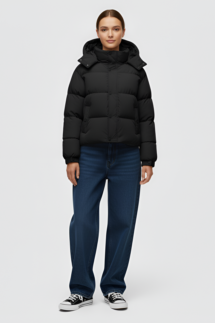 Woman wearing a black puffer jacket and cap standing in an urban setting.