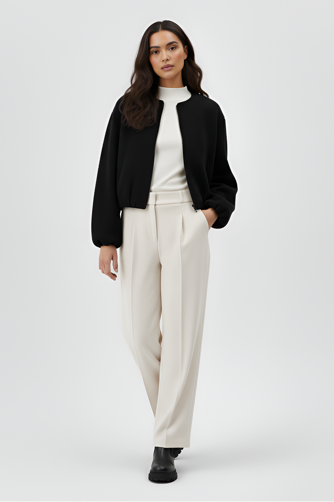 Woman wearing a black jacket, white shirt, and beige pants on a white background