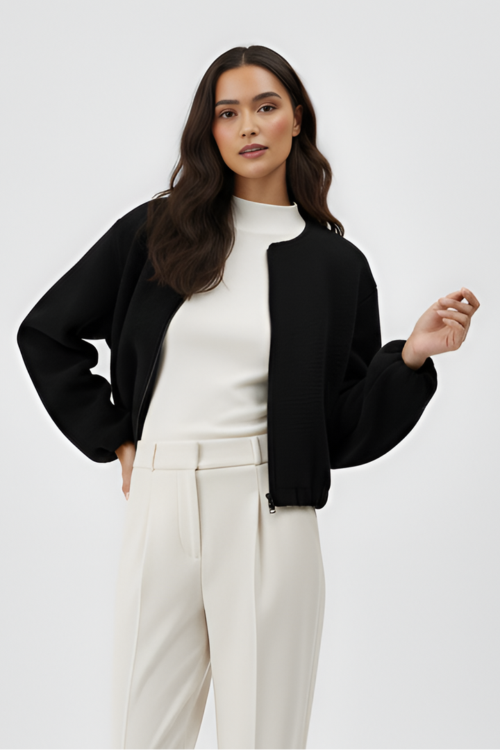 Woman wearing a black jacket, white top, and beige pants on a white background
