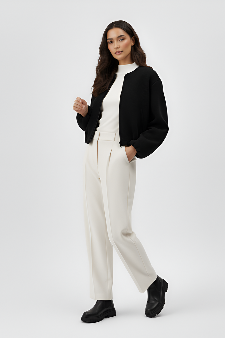 Woman wearing a black jacket, white top, and white pants on a white background