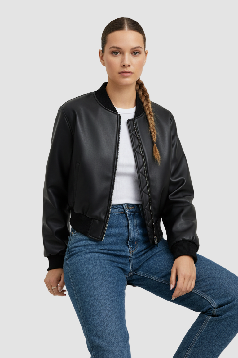 Woman wearing a black leather bomber jacket and blue jeans on a light gray background
