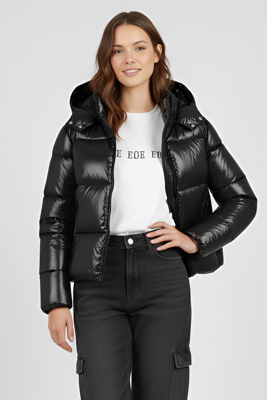 Woman wearing a black puffer jacket, white shirt, and black pants on a light gray background