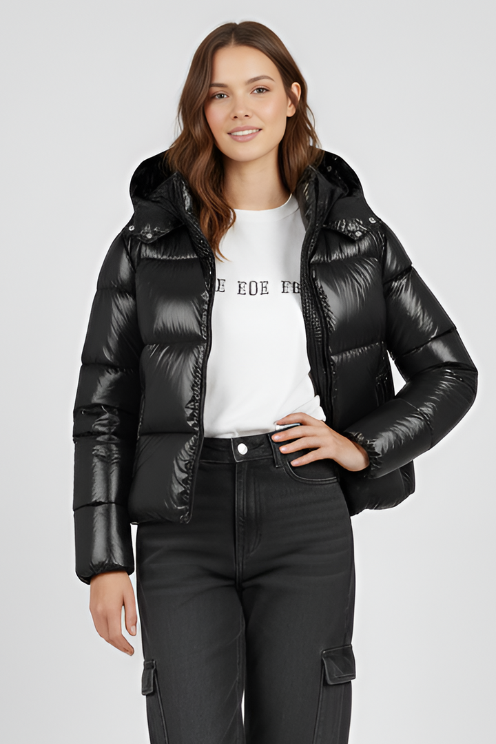 Woman wearing a black puffer jacket, white shirt, and black pants on a light gray background