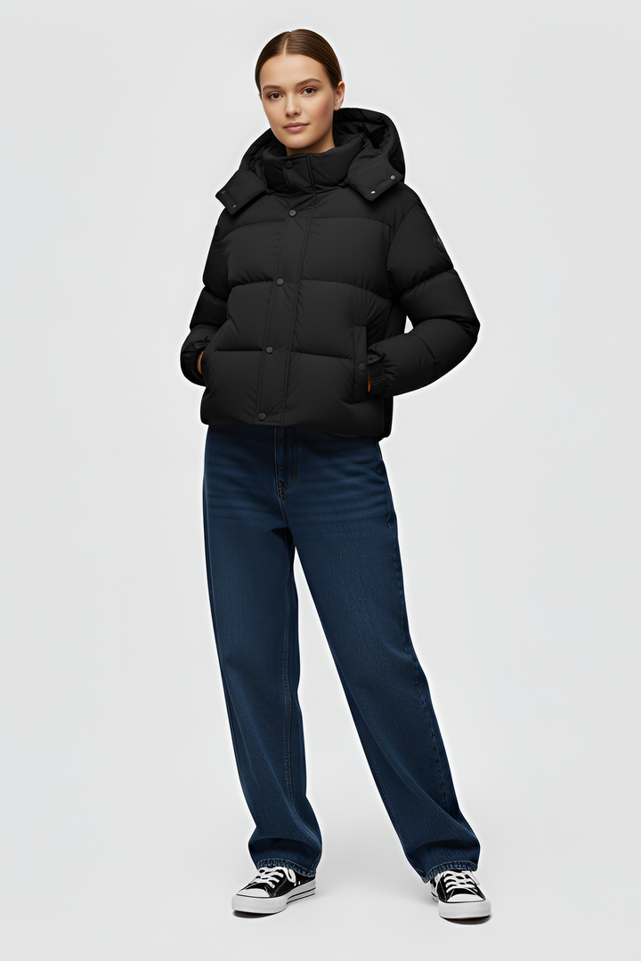 Woman wearing a black puffer jacket and cap standing in an urban setting.