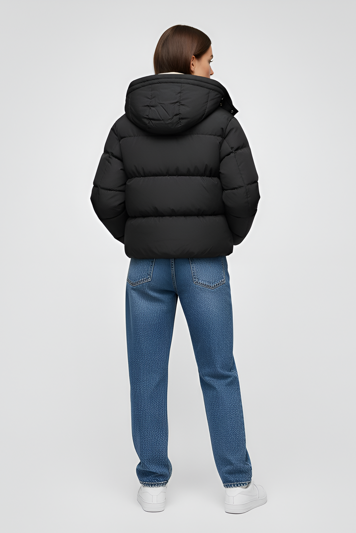 Woman wearing a black puffer jacket, black hoodie, beige cargo pants, and white sneakers on a light gray background