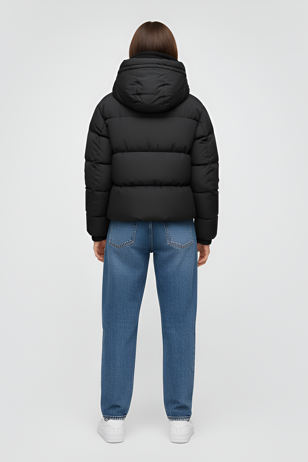 Woman wearing a black puffer jacket over a pink hoodie with black pants on a white background