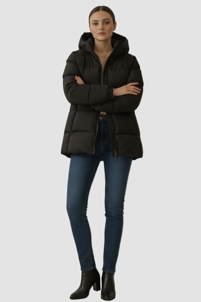Woman wearing a black puffer jacket, blue jeans, and black boots on a plain background
