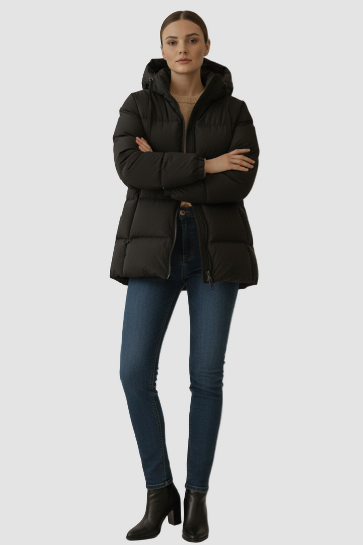 Woman wearing a black puffer jacket, blue jeans, and black boots on a plain background