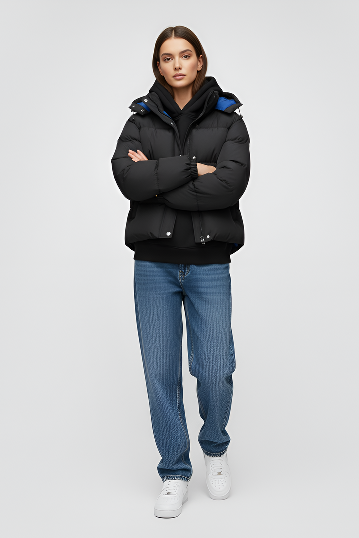 Woman wearing a black puffer jacket over a pink hoodie with black pants on a white background