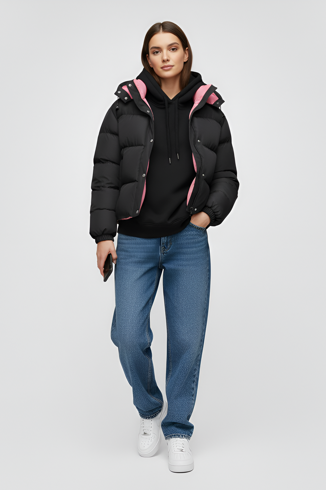 Woman wearing a black puffer jacket over a pink shirt with a white background