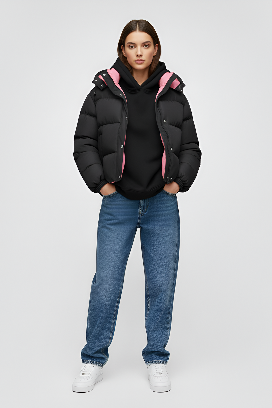 Woman wearing a black puffer jacket over a pink shirt with a white background