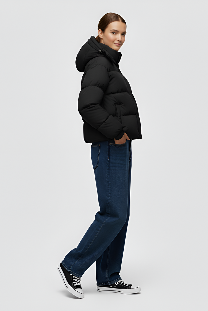 Woman wearing a black puffer jacket and cap standing in an urban setting.