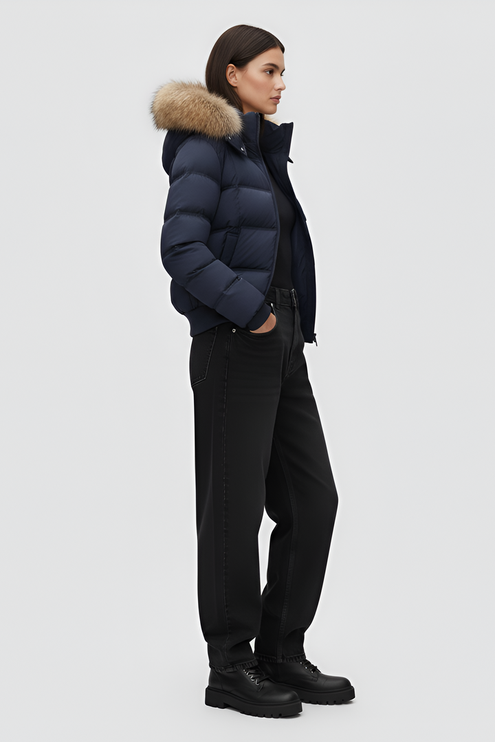 Woman wearing a blue puffer jacket, white shirt, and gray pants on a plain background