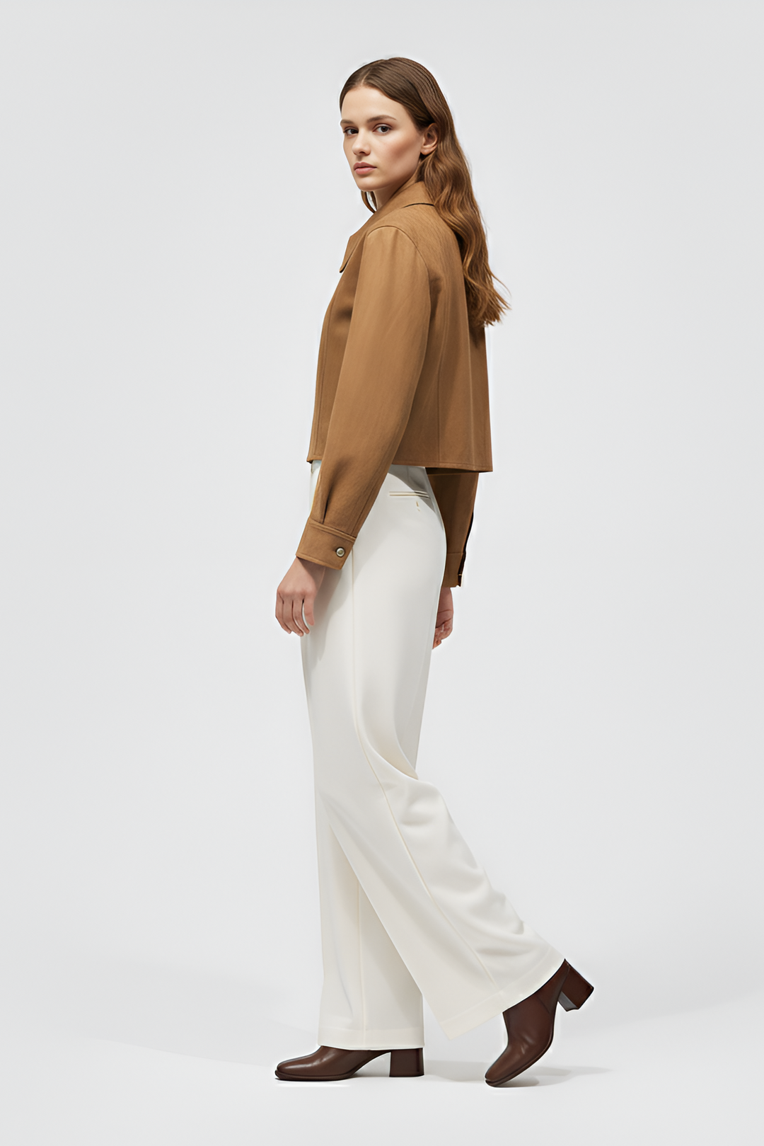 Woman wearing a brown blouse and white pants on a light gray background