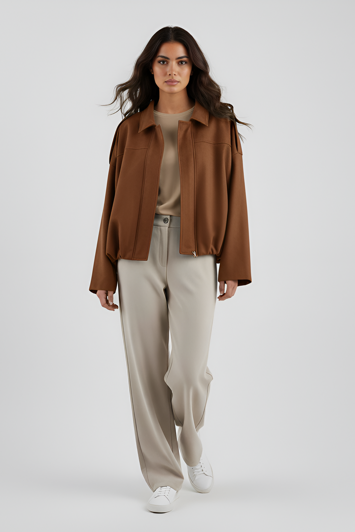 Woman wearing a brown jacket, beige top, and light gray pants on a white background