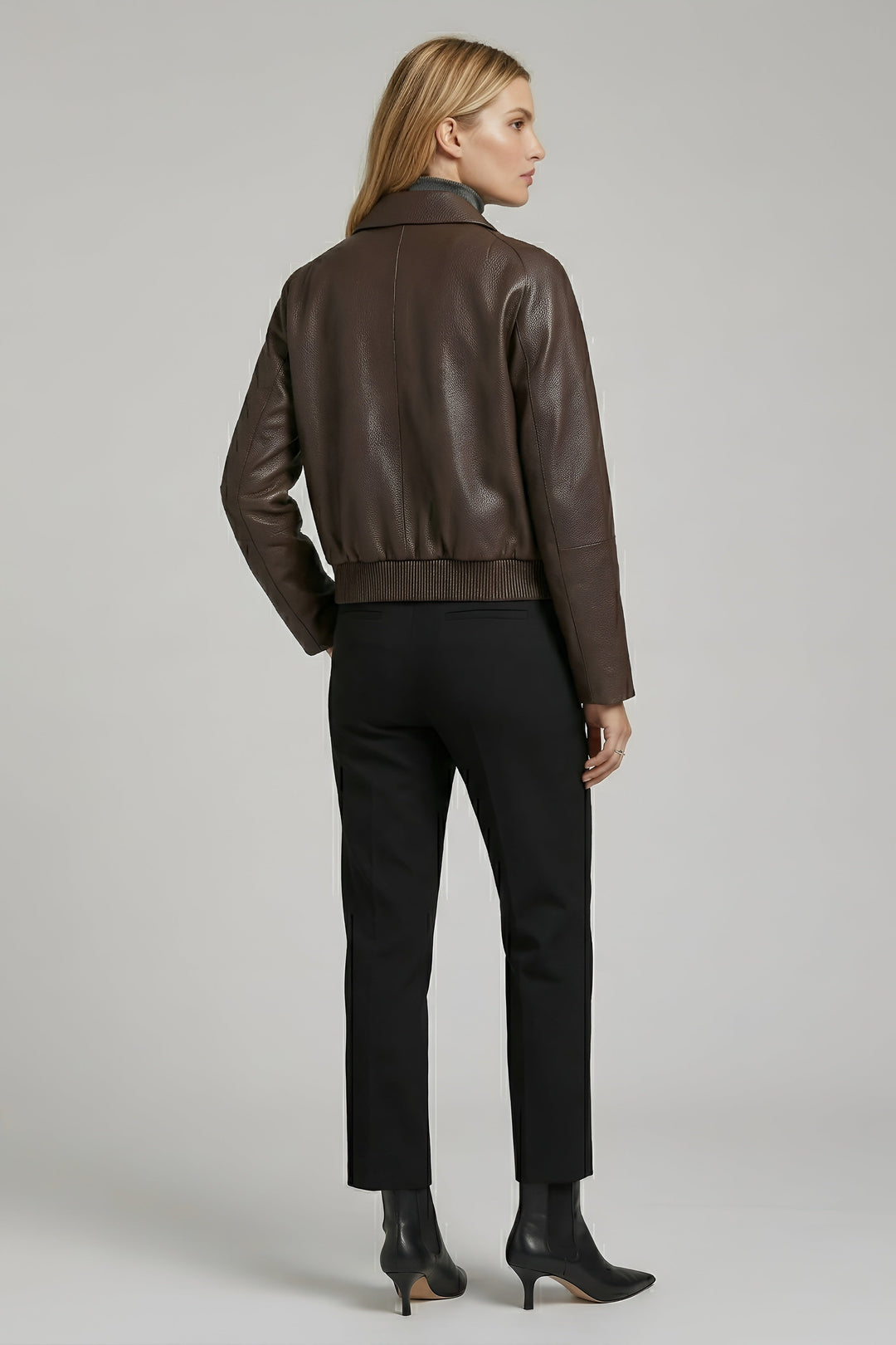 Woman wearing a brown leather jacket and black pants on a gray background