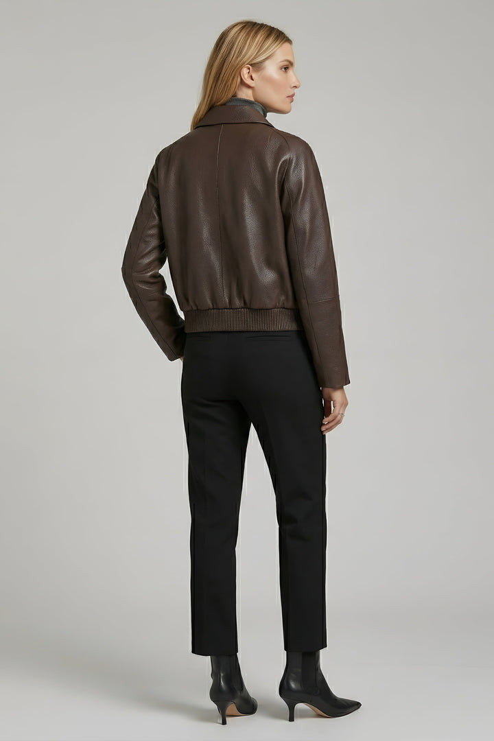 Woman wearing a brown leather jacket and black pants on a gray background