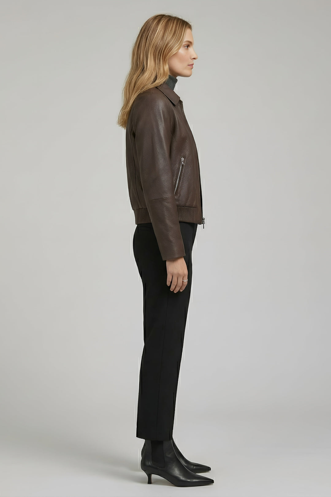 Woman wearing a brown leather jacket and black pants on a plain background