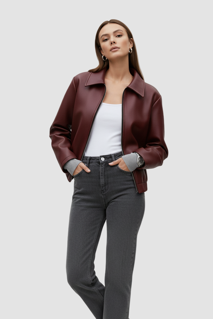 Woman wearing a brown leather jacket, white top, gray jeans, and black boots on a plain background