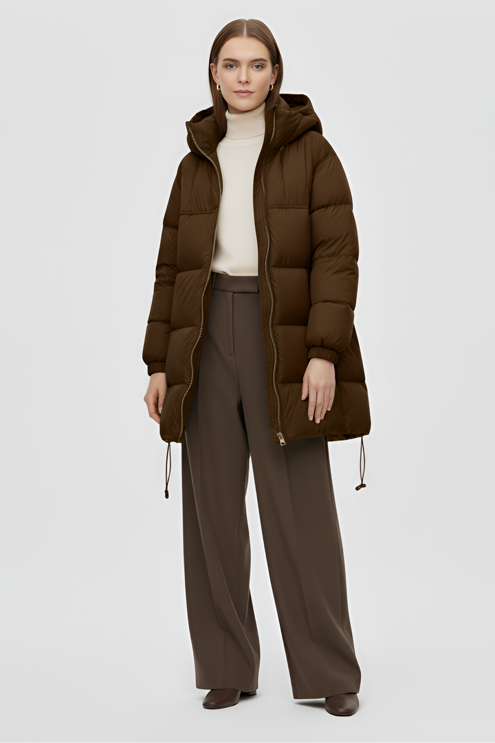 Woman wearing a brown puffer coat and dark pants on a light gray background