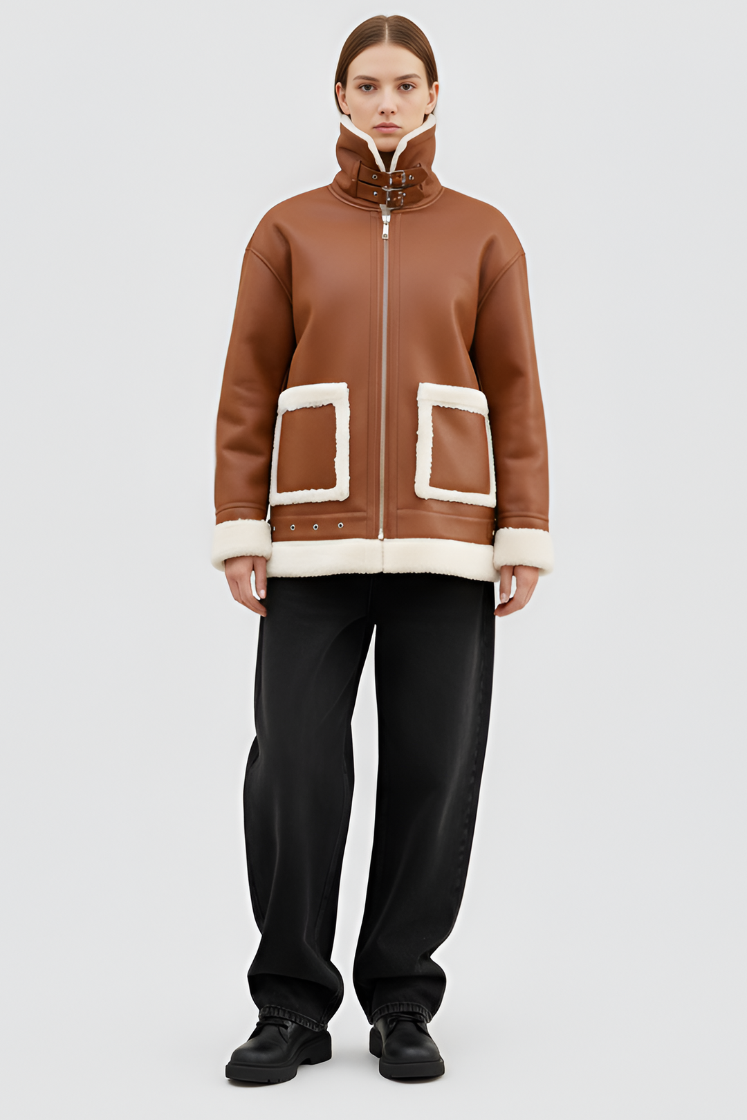Woman wearing a brown shearling coat with white trim on a plain background
