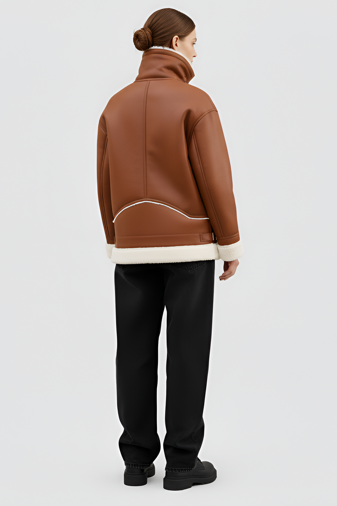 Woman wearing a brown shearling coat with white trim on a plain background