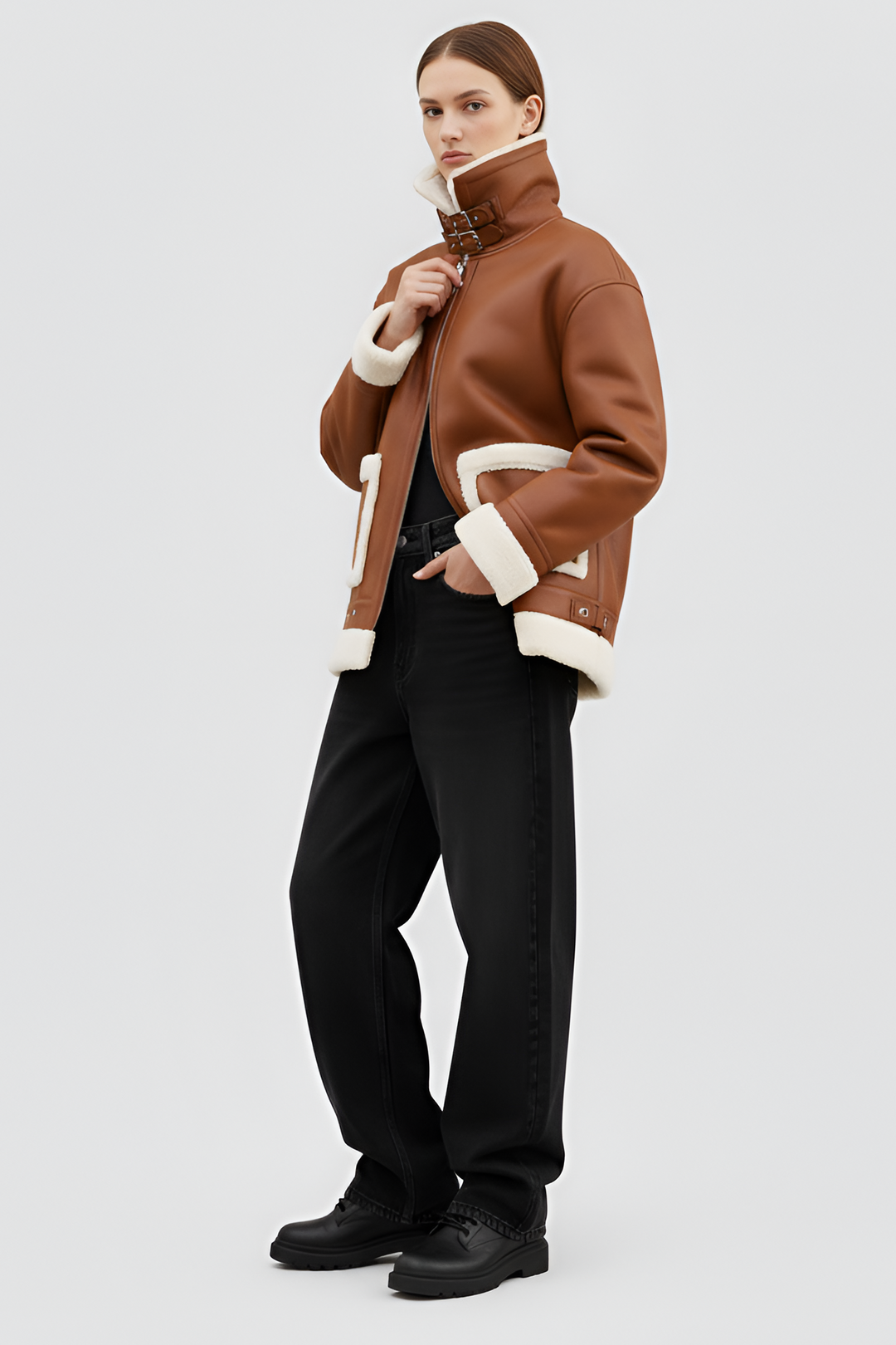 Woman wearing a brown shearling coat with white trim on a plain background