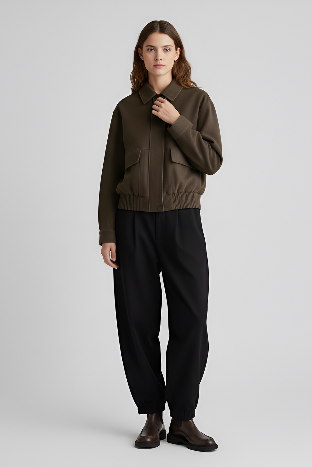 Woman wearing a brown sweater and black pants on a light gray background