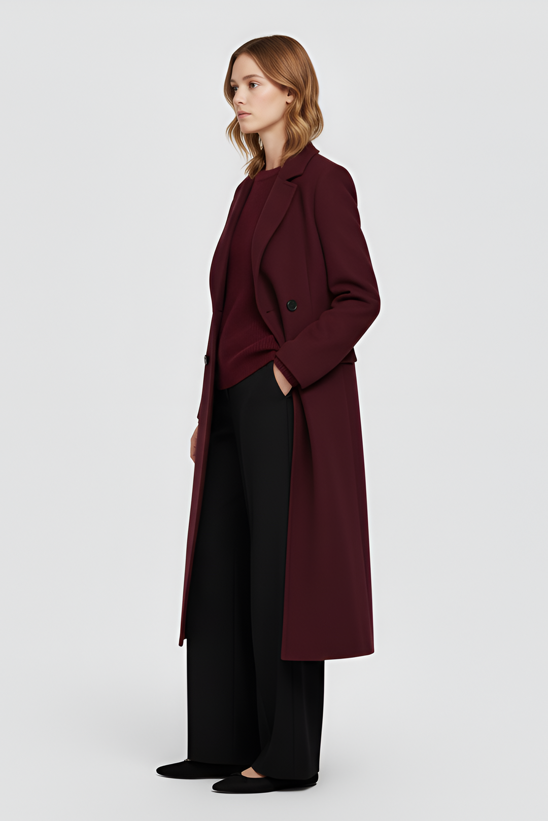 Woman wearing a burgundy coat and black pants on a white background