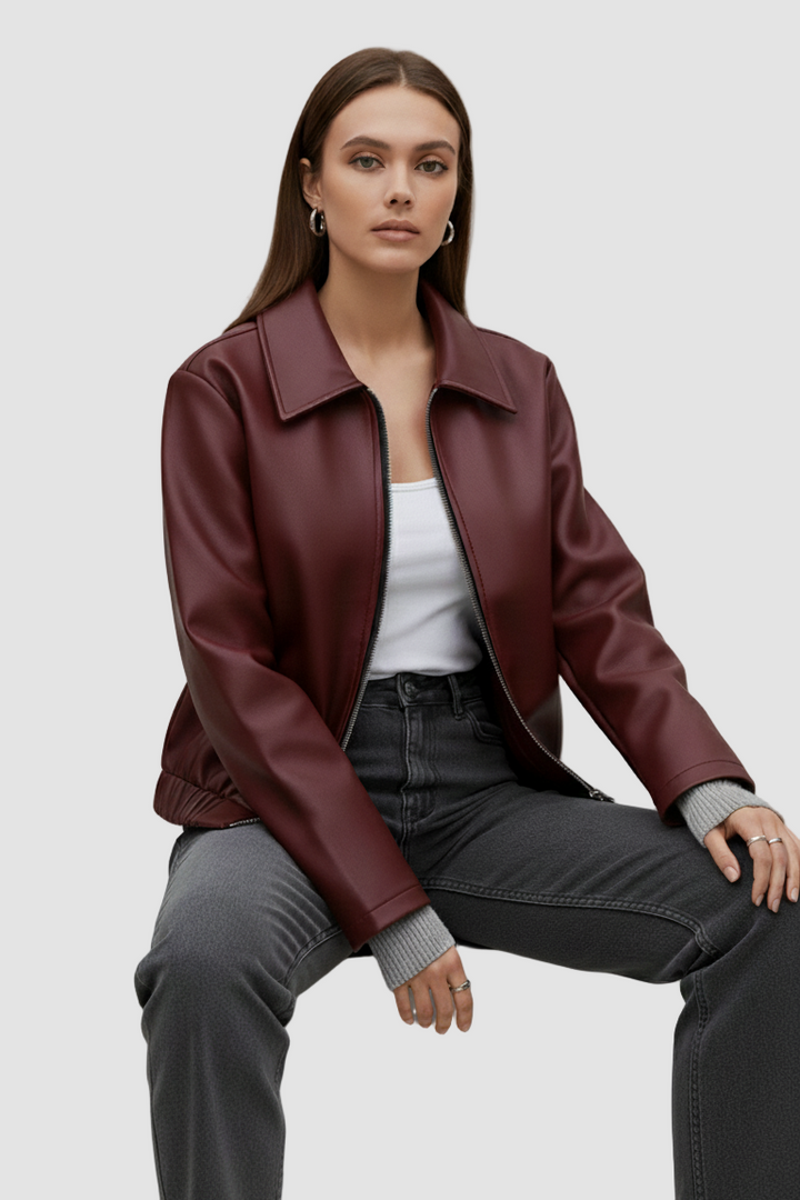 Woman wearing a burgundy leather jacket sitting on a gray block against a plain background