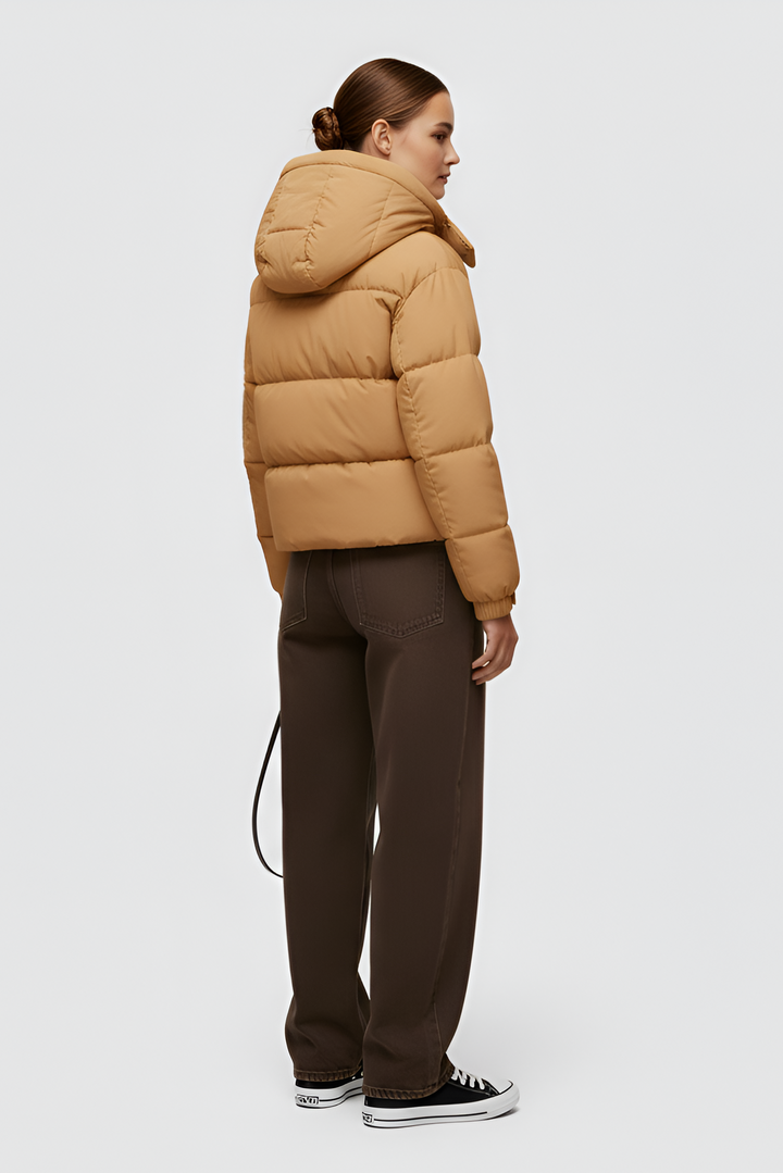 Woman wearing a camel puffer jacket and cap standing in an urban setting.