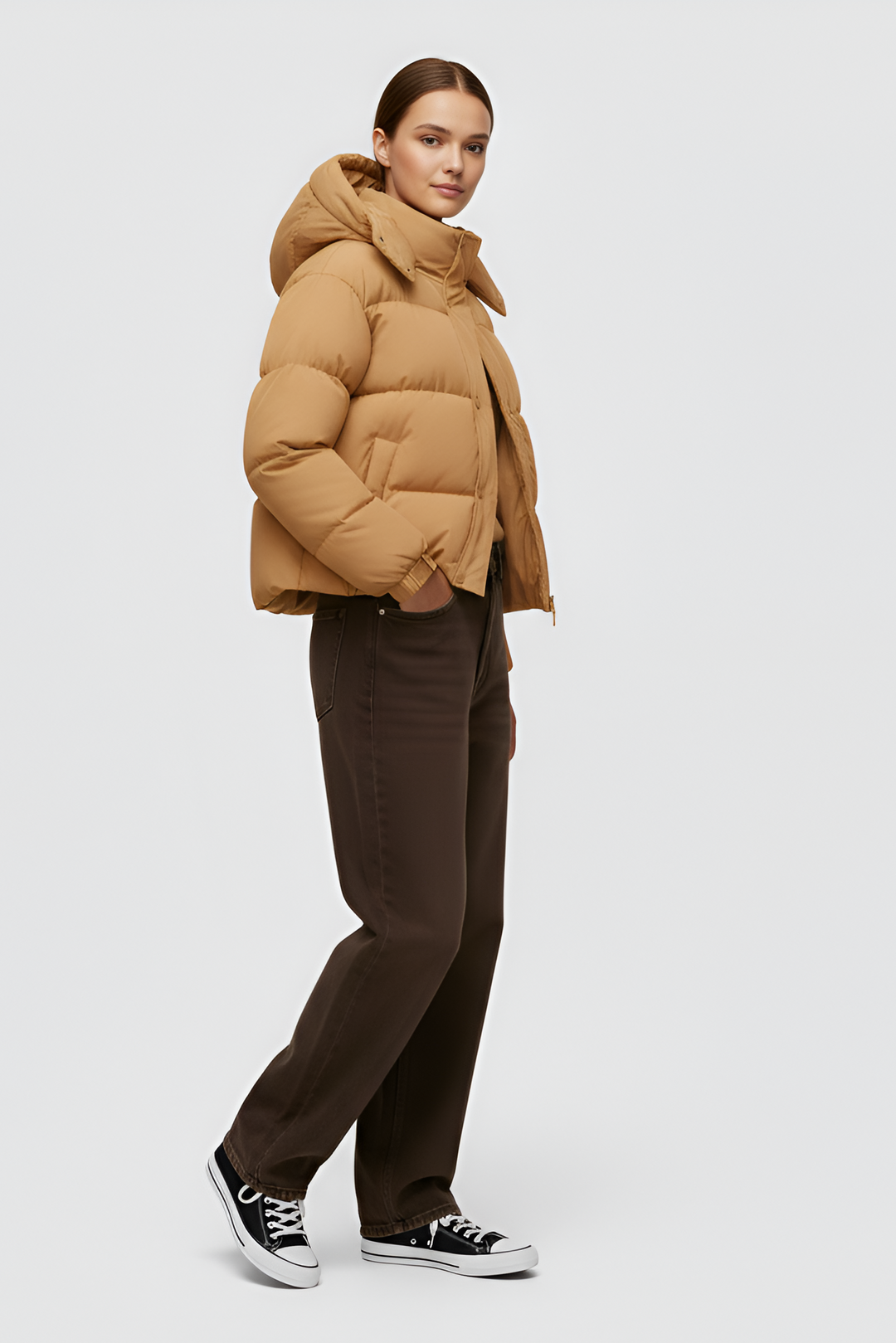 Woman wearing a camel puffer jacket and cap standing in an urban setting.