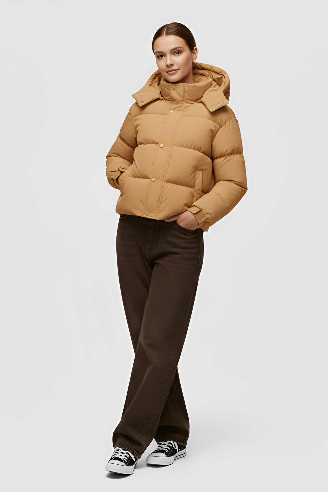 Woman wearing a camel puffer jacket and cap standing in an urban setting.