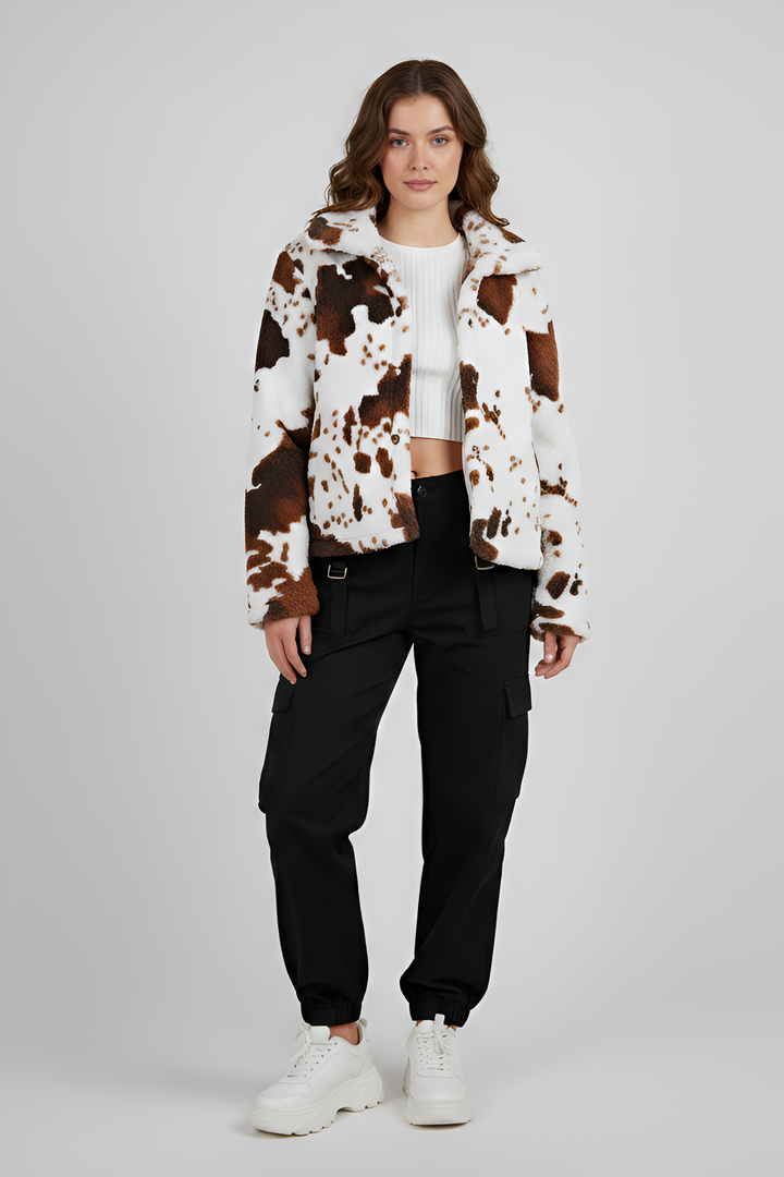 Woman wearing a cow print jacket and black pants on a gray background